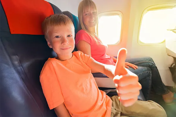 Child sitting next to his mother on a plane gives the thumbs up to the camera. 