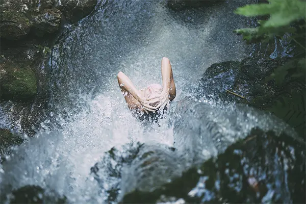 Woman showering underneath a waterfall. 