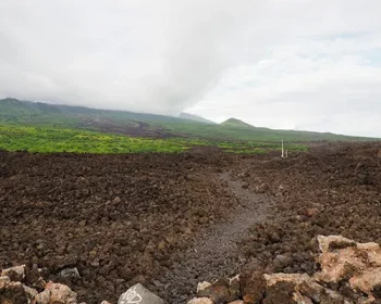 Hoapili trail on a cloudy day on Maui, a dirt path and a grassy hill in the distance.