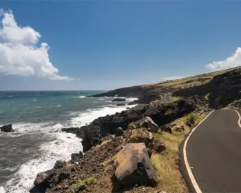 A picture of a road in Maui that runs alongside the shore.