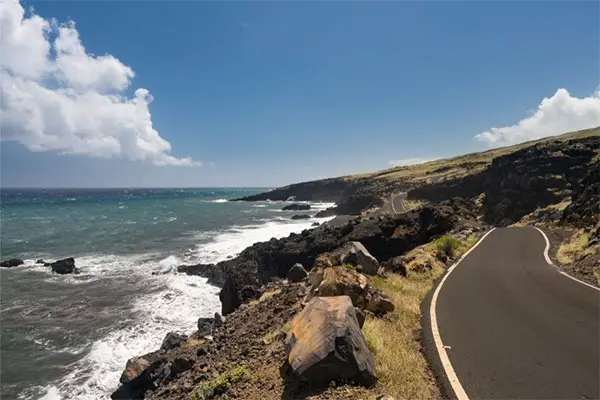 A picture of a road in Maui that runs alongside the shore. 