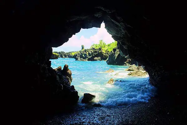 A sea cave during the day, as warm blue water rushes into a hidden cave. 