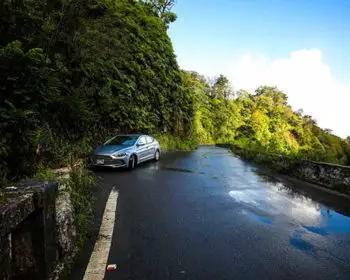 A rental car is stopped on the side of the famous Road to Hana near a trail leading to a waterfall.