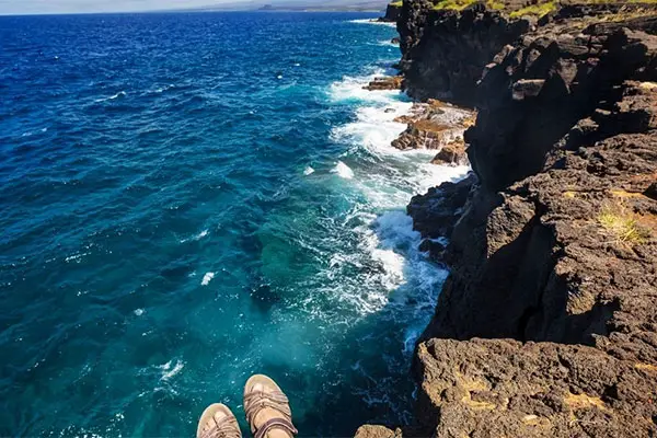 Person's feet hanging over the edge of a cliff overlooking the ocean. 