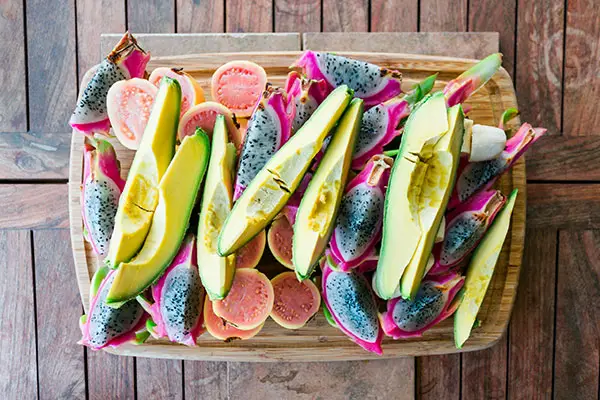 A platter with avocado, passion fruit, and dragon fruit on a wooden table.