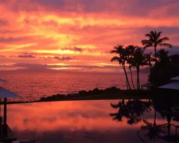 Orange and golden sunset from a cabana-side pool overlooking the ocean.