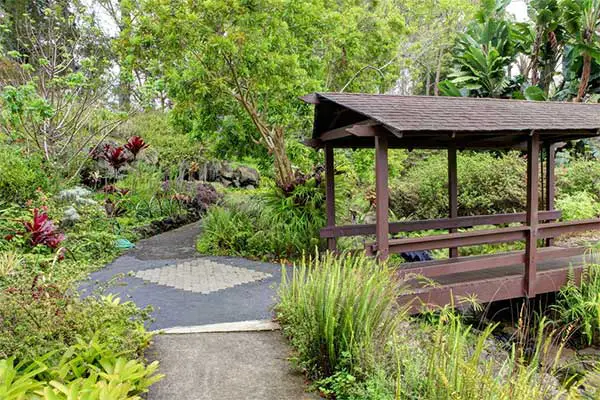 Garden path in Kula maui featuring lush vegetation and a shaded bridge. 