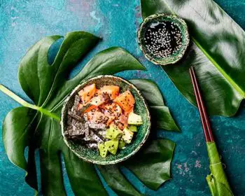 Hawaiian salmon poke poce with avocado, rice and sesamo served in bowls on tropical leaves. Sushi