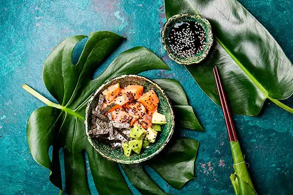 Hawaiian salmon poke poce with avocado, rice and sesamo served in bowls on tropical leaves. Sushi