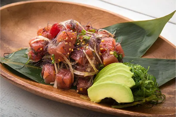 Poke on a wooden plate with sliced avocado.