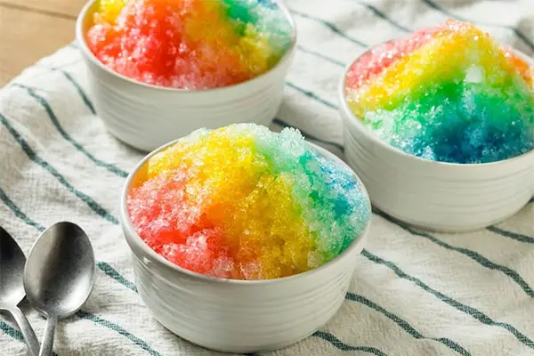 Rainbow shave ice on a striped cloth. 