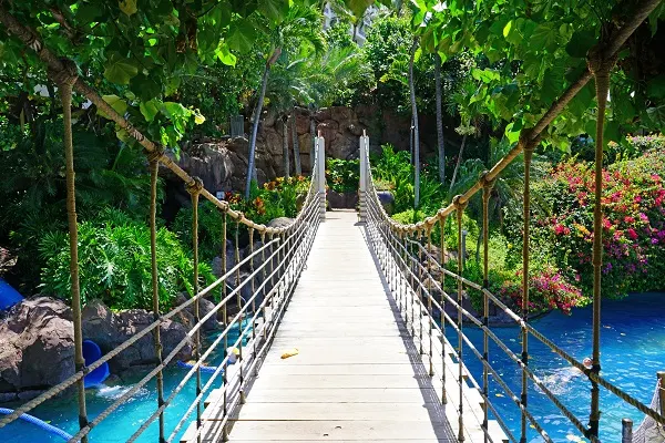 A wooden suspension bridge crossing clear blue water on a resort in Maui.