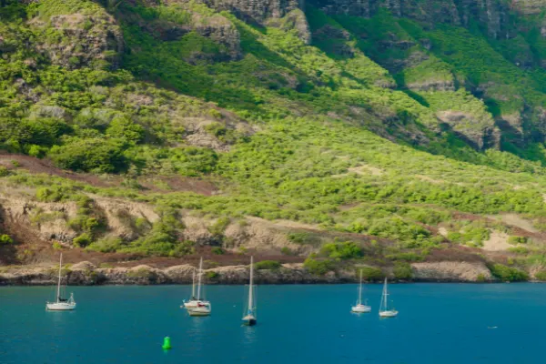 Boats in the ocean just beneath the hills of an island.