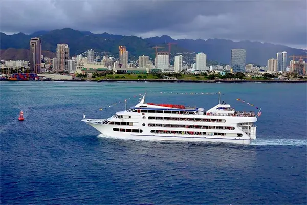 Cruise ship sailing near shore with a city skyline beyond.