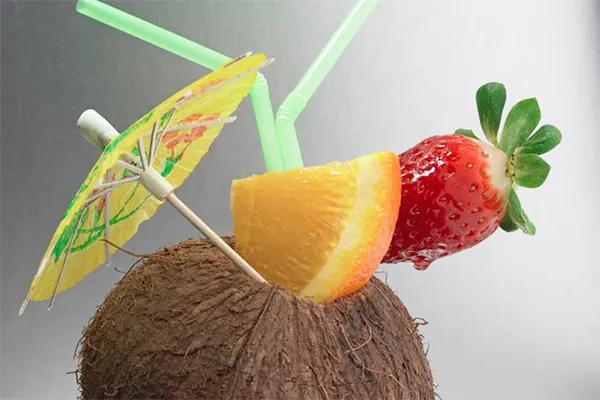 Tropical coconut drink with orange wedge, strawberry, and umbrella. 