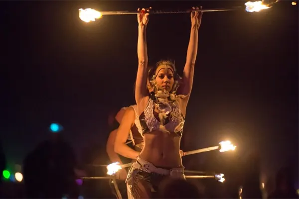 Woman firedancer holding pole on fire above her head. 