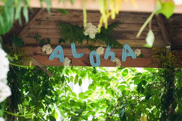 The word Aloha in lettering across gazebo wall with vegetation behind it. 