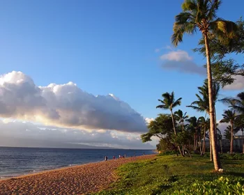 Kaanapali Beach at Dusk with gentle waves, people, hotels and trees. Island of Lanai can be seen in the distance on Maui, Hawaii.