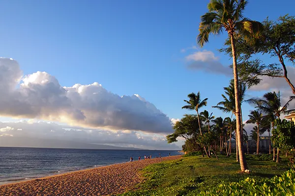 Kaanapali Beach at Dusk with gentle waves, people, hotels and trees. Island of Lanai can be seen in the distance on Maui, Hawaii.