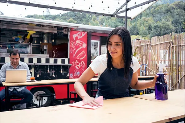 Woman near food truck cleaning tables with rag.