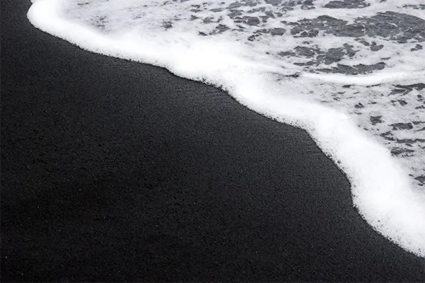 The tide flowing up black sand at one of Maui's black sand beaches.