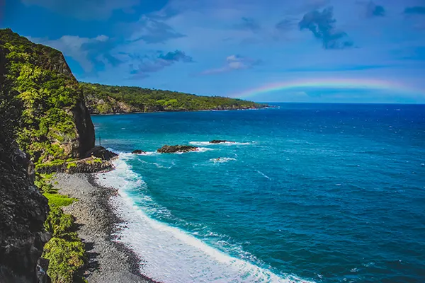 Waves crashing a Maui Beach with a rainbow in the distance on the Road To Hana, Maui, Hawaii