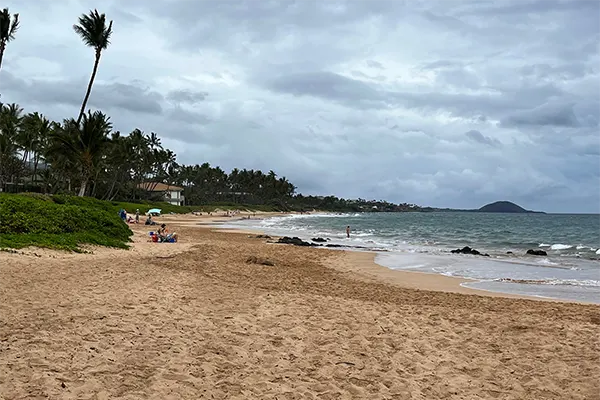 Wide shot of Keawakapu Beach on a cloudy day, people tanning and wading into the water. 