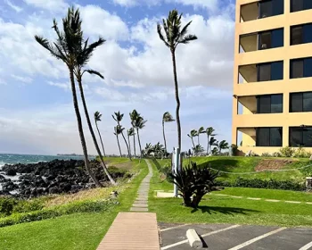 Outside view of Kihei Surfside condo with parking lot and ocean in background.