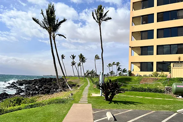 Outside view of Kihei Surfside condo with parking lot and ocean in background. 