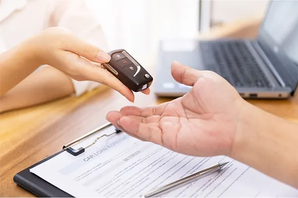 Person handing car keys over a desk. 