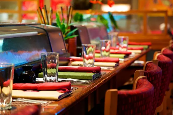 A sushi restaurant, chairs and plates and napkins before the sushi bar.