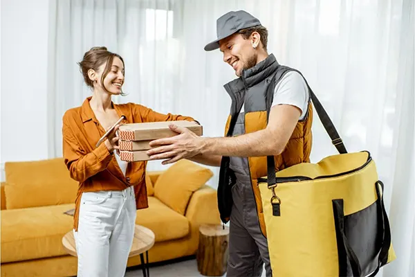 Pizza delivery man handing pizza off to smiling lady.