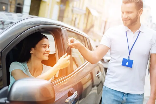 Woman accepting keys from man while sitting in driver's seat of the car. 