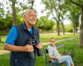 A senior man in the park holding binoculars by his chest.