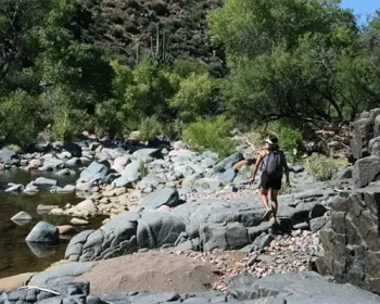 Person with backpack crossing a stream on the 13 Crossings trail.