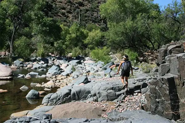 Person with backpack crossing a stream on the 13 Crossings trail. 