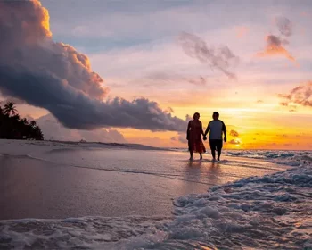 Couple standing on beach at sunset.