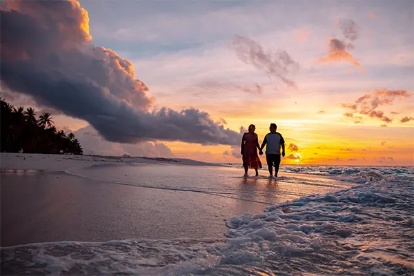 Couple standing on beach at sunset. 