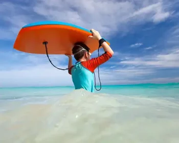 Boy holding boogie board over his head as he wades into the ocean.