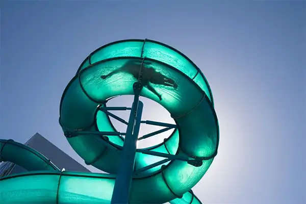 Looking up at a teal waterslide, a man in the tube going down the slide. 