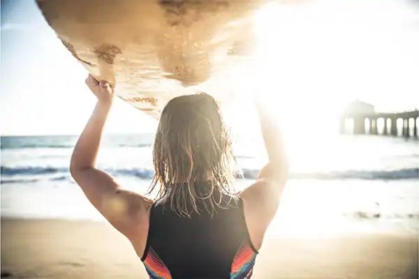 Woman holding surfboard over her head at the beach. 