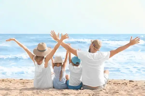 A family of four sitting on the beach, watching the tide come in, their hands spread wide in the air. 