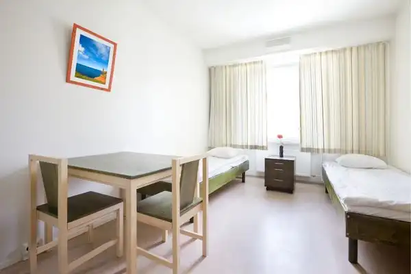 A sparse hostel room, with two beds and a small table. 