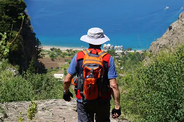 Man wearing a backpack hiking down a hill towards the ocean. 