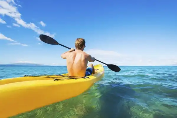 Man in a yellow kayak paddling in the ocean.