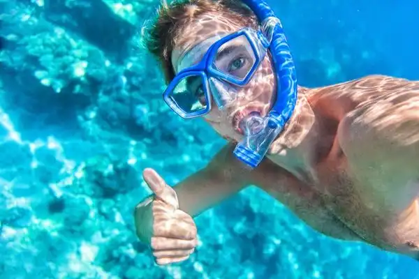 Man wearing snorkeling gear, underwater, giving the thumbs up.